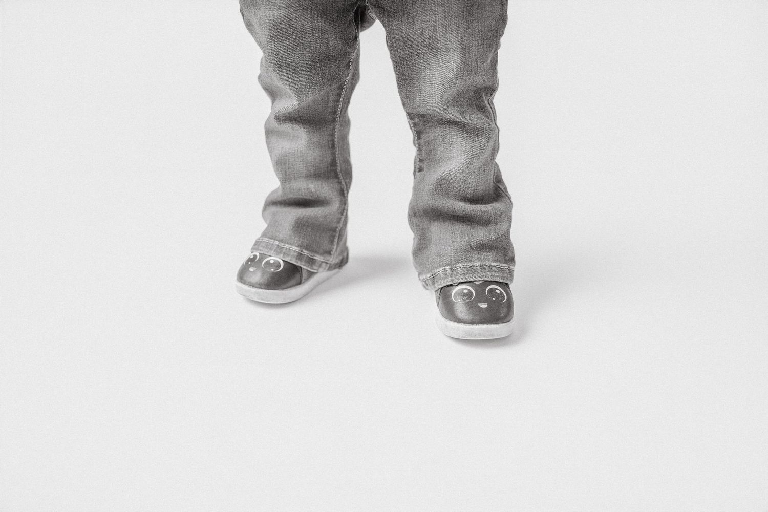 Black and white photo of toddler legs wearing jeans and cute squeaky character sneakers.