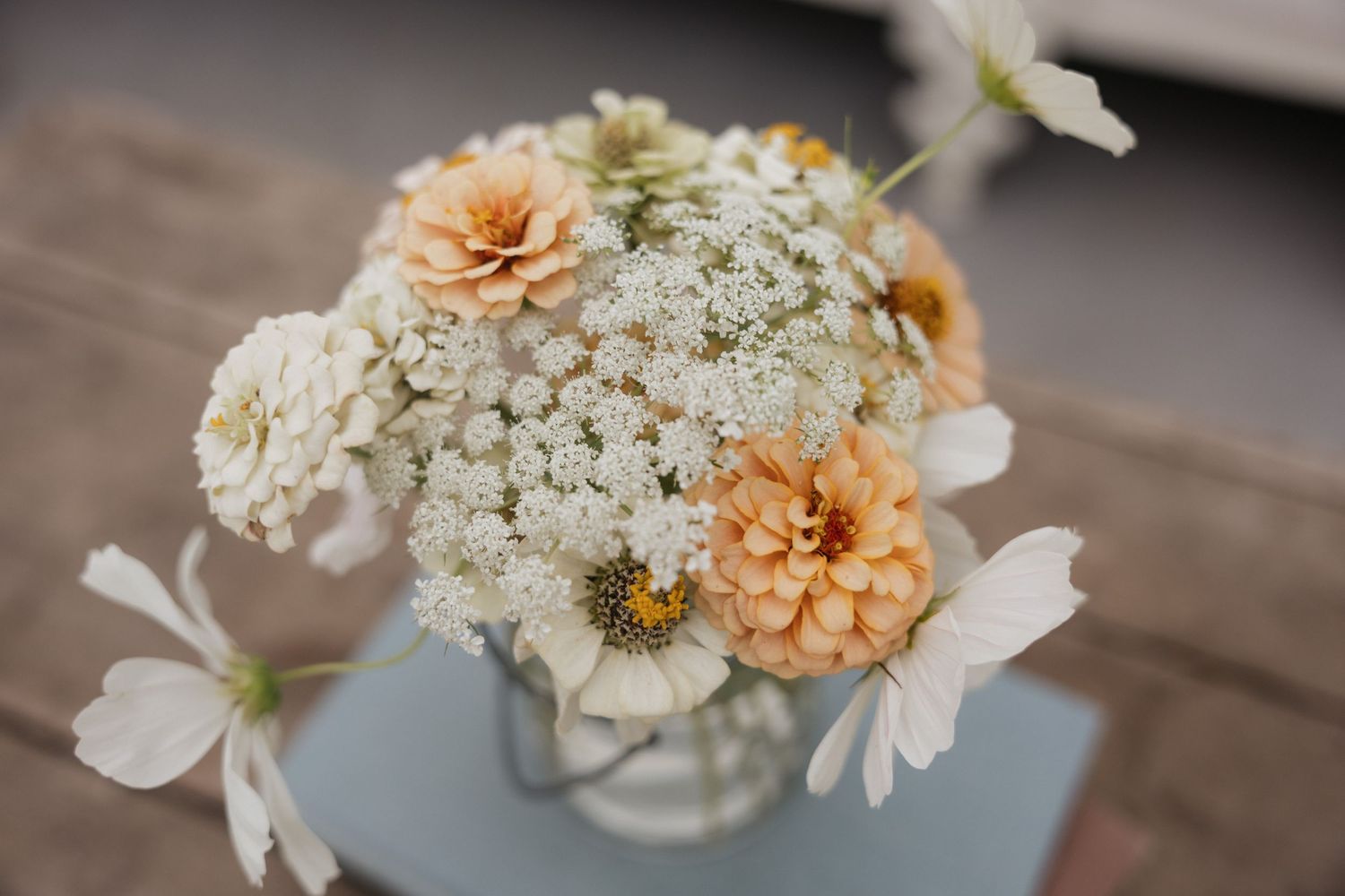 Top-down view of a rustic bouquet with white Queen Anne's lace, peach zinnias, and white cosmos in a glass vase.