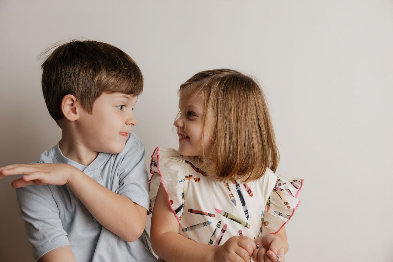 Two young children smiling and hugging each other against a light background.