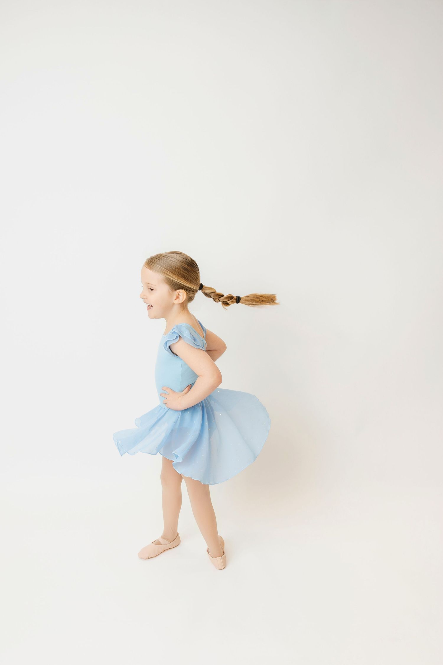 Young girl in a blue ballet dress twirling with a long braid flying behind her.
