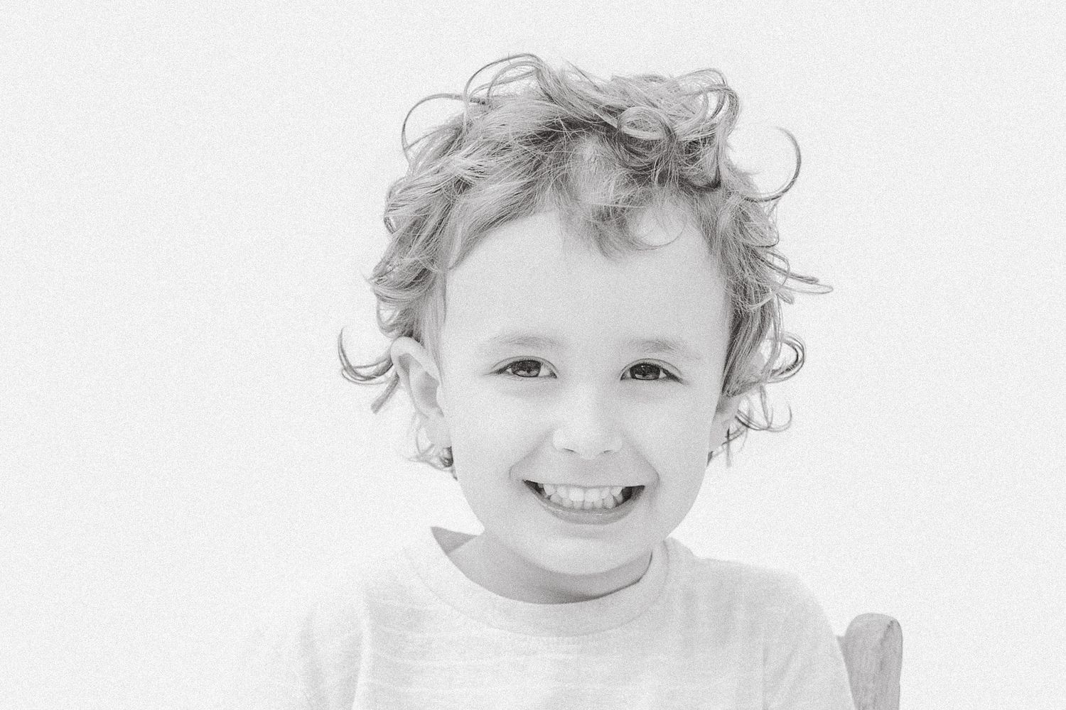 Close-up black and white portrait of a curly-haired child with a bright cheerful smile.