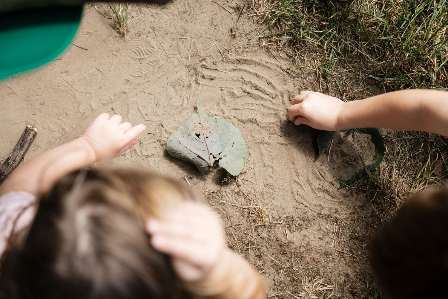 Children playing in a sandbox with rocks and sand imprints during outdoor nature play activity.