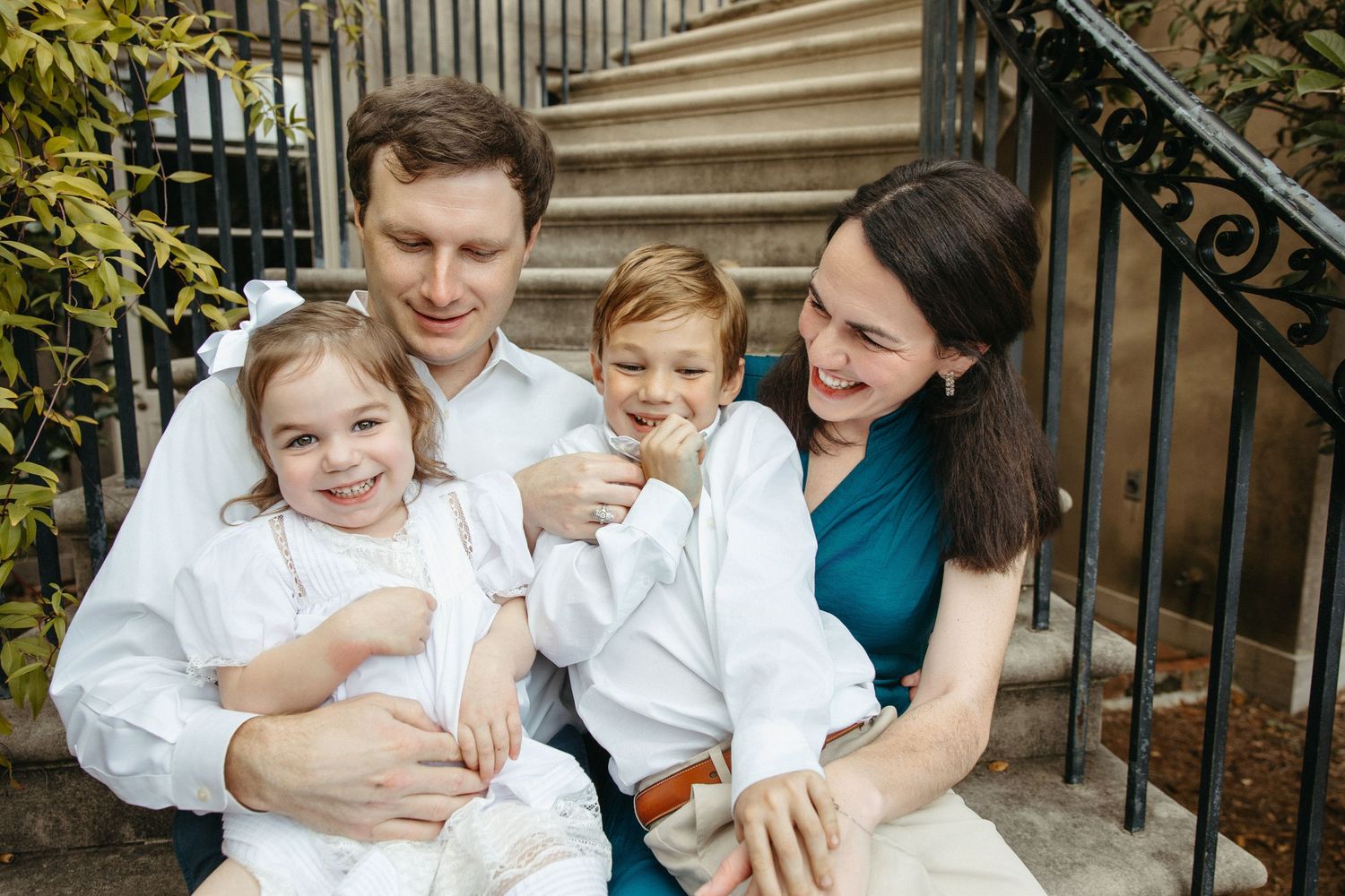 Happy family of four sitting on outdoor steps smiling and laughing together.