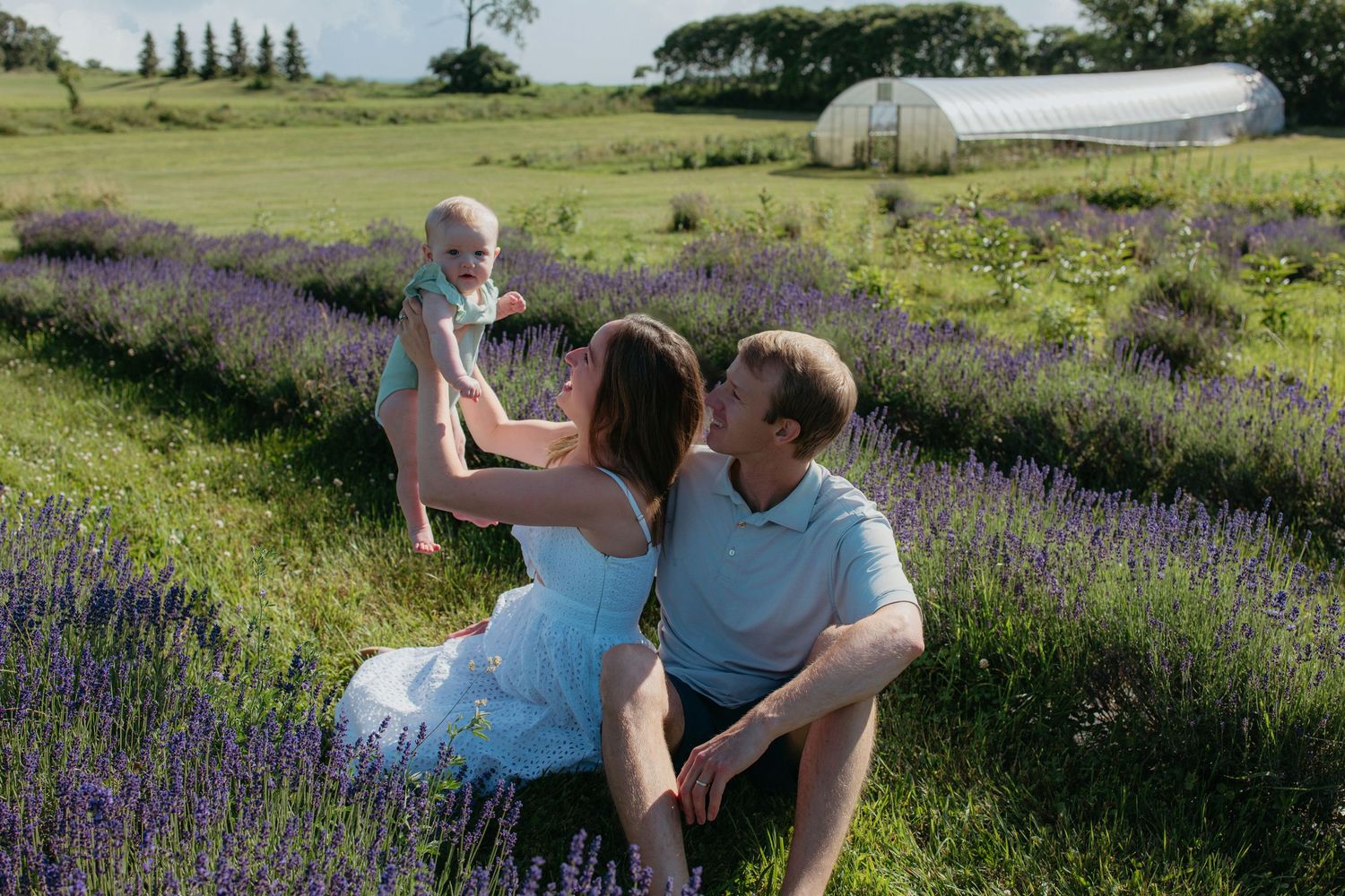 Young couple sitting in a lavender field, sharing a tender moment while holding their baby.