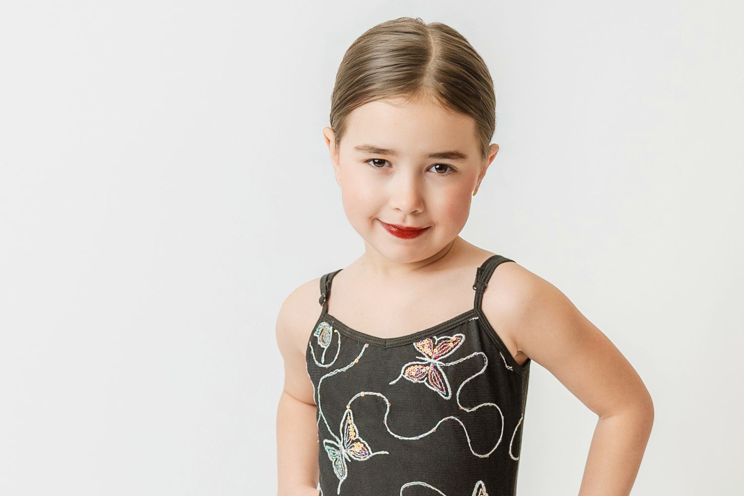 Young girl in a dark butterfly print dance leotard posing with hand on hip.