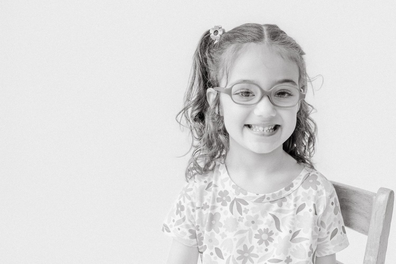 Smiling young girl with glasses and pigtails in a black and white portrait photo.