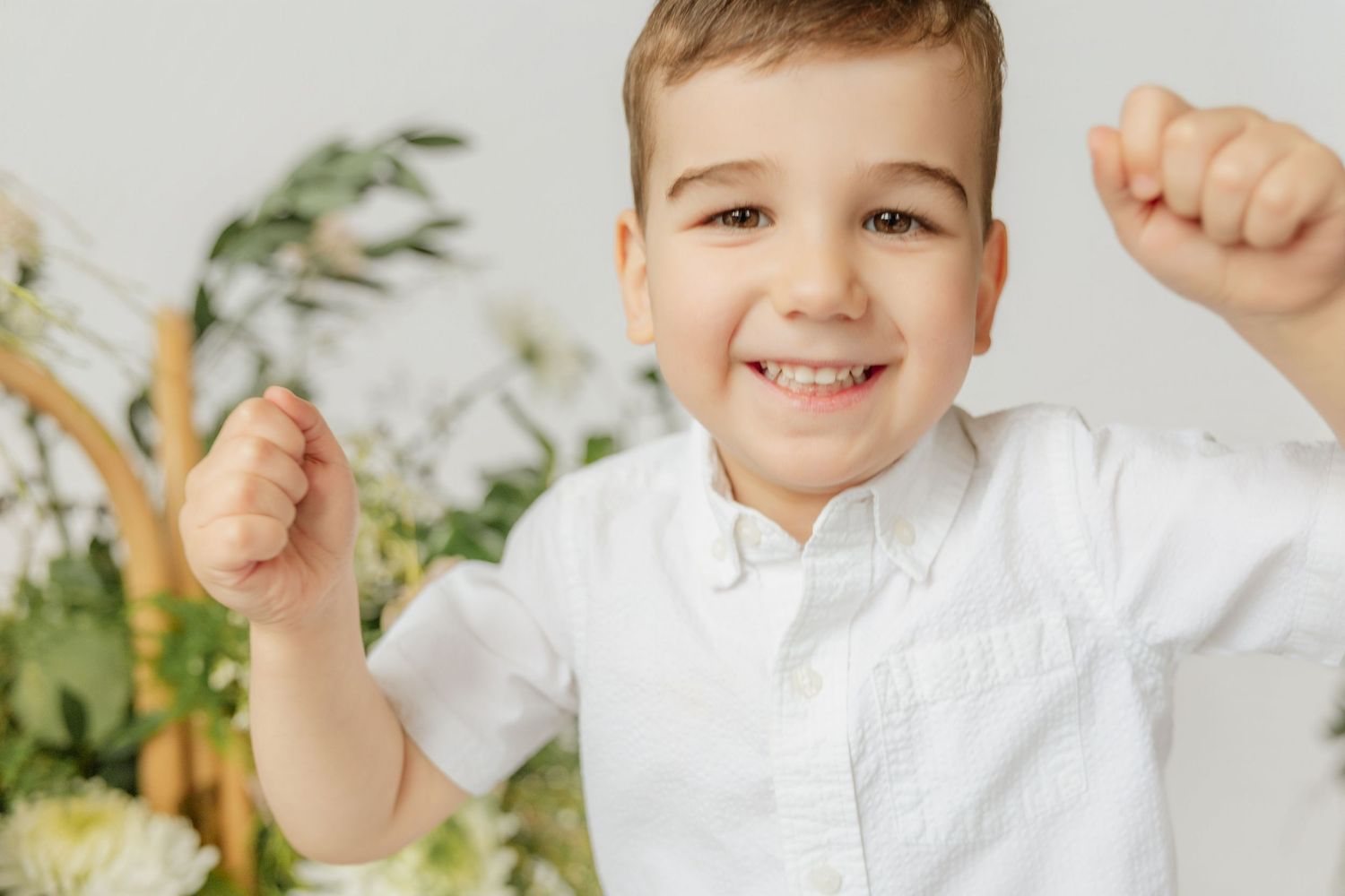 Excited young boy in white shirt celebrating with fists raised, surrounded by flowers.