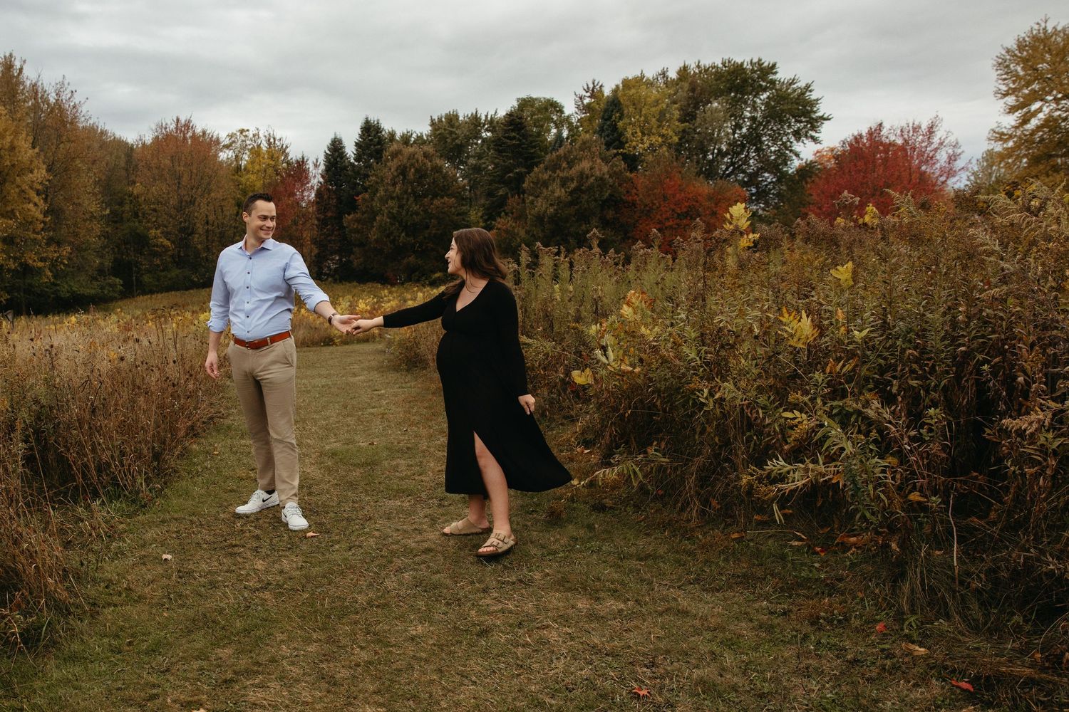 Joyful couple holding hands and dancing in a scenic autumn meadow with vibrant fall-colored trees.
