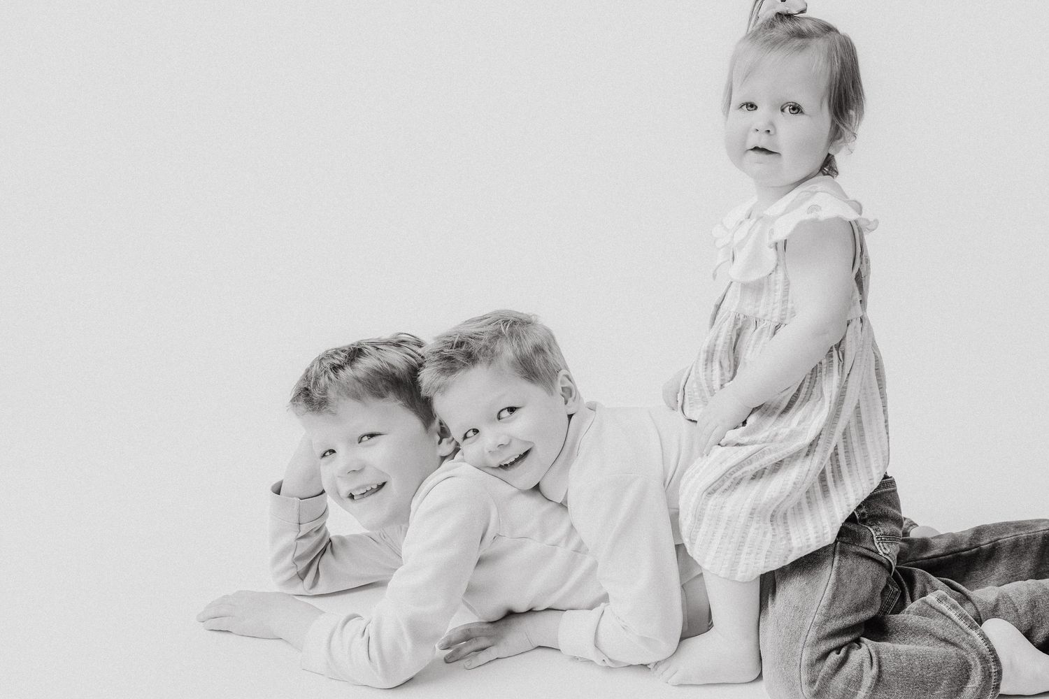 Black and white portrait of three siblings posing together, two boys lying down and girl sitting.
