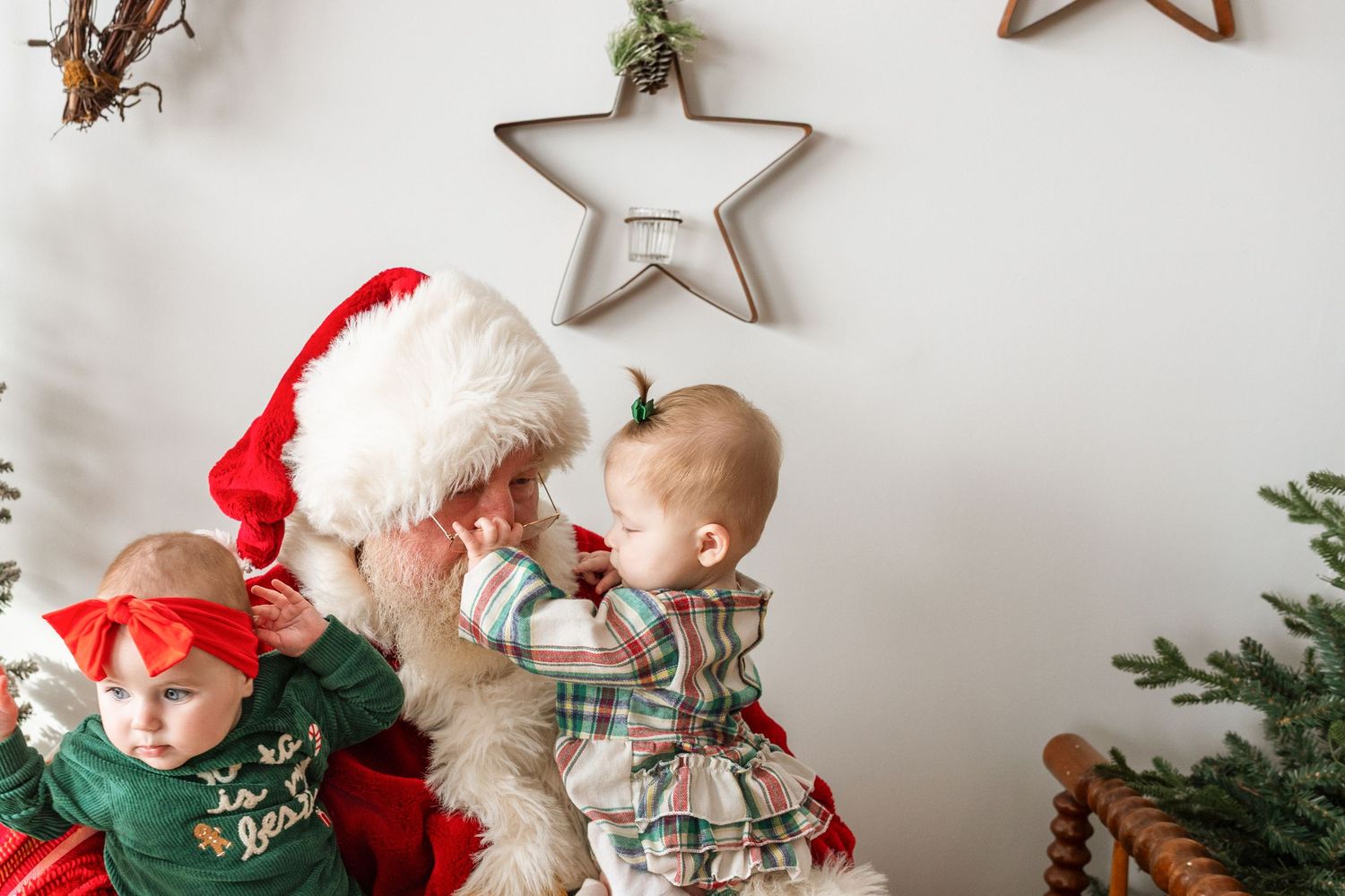 Two adorable babies in holiday outfits interact with Santa Claus during a Christmas portrait session.