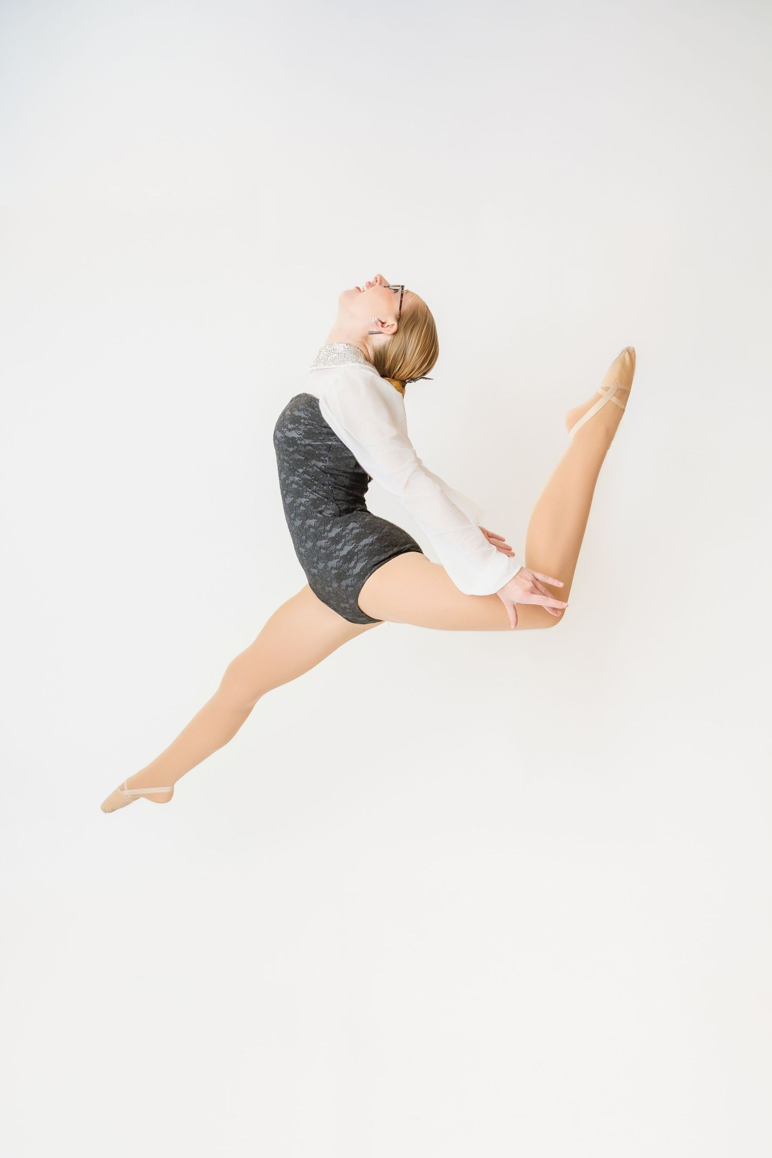 Teen dancer leaps gracefully in mid-air wearing white top and gray shorts against white background.