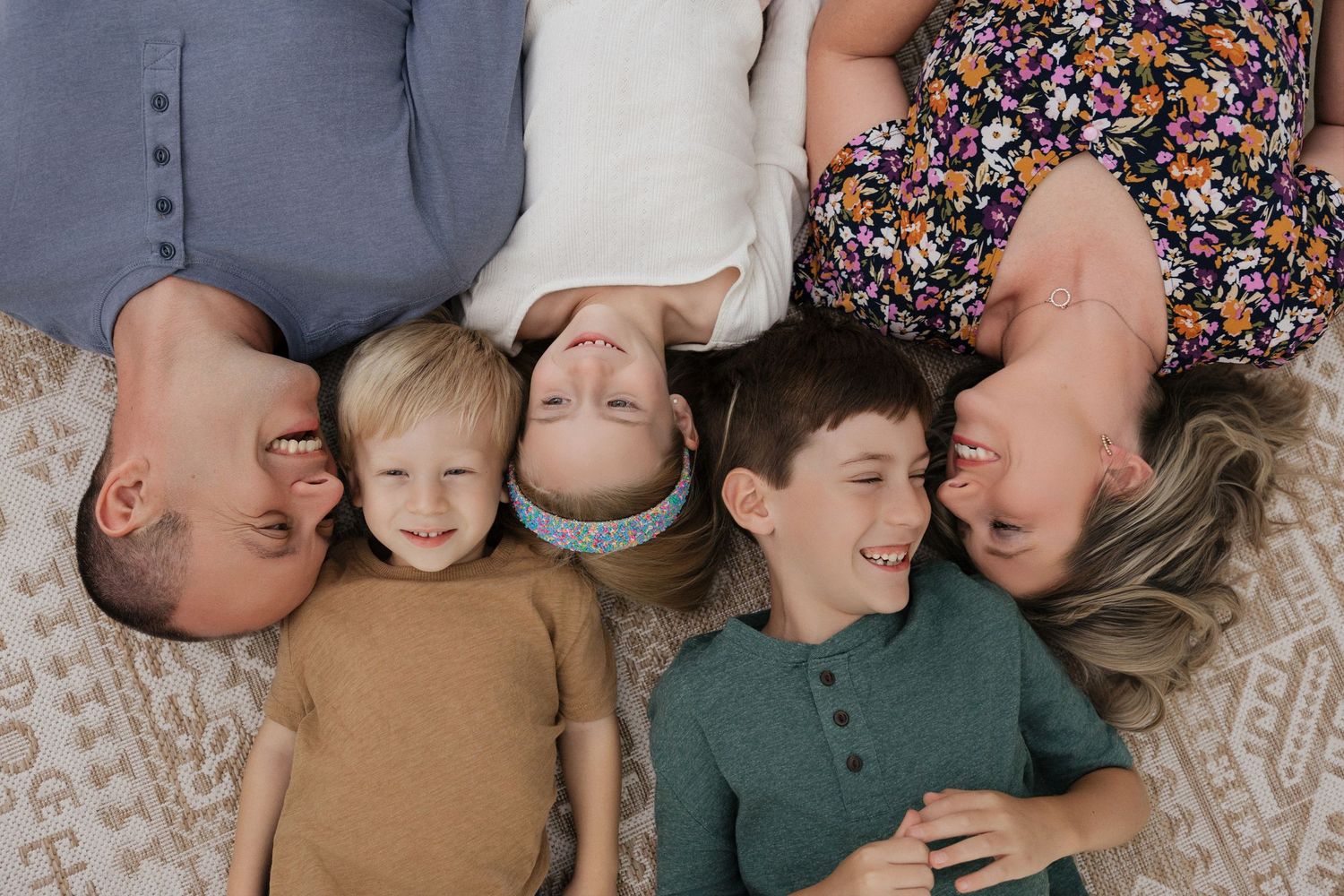 Family of five lying on floor smiling, two parents with three young children in casual portrait photo.