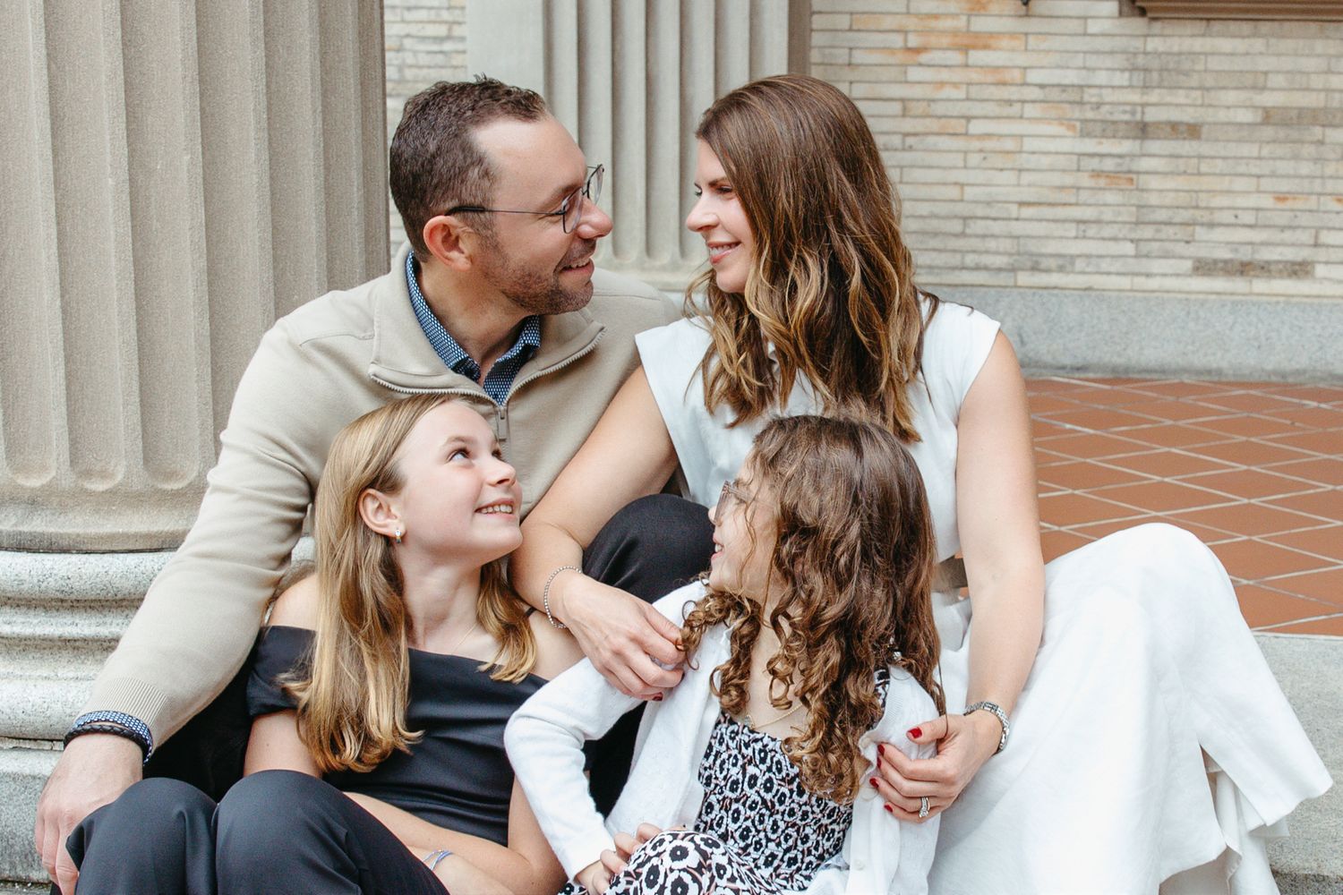 Loving family of four sitting together on steps near stone columns.