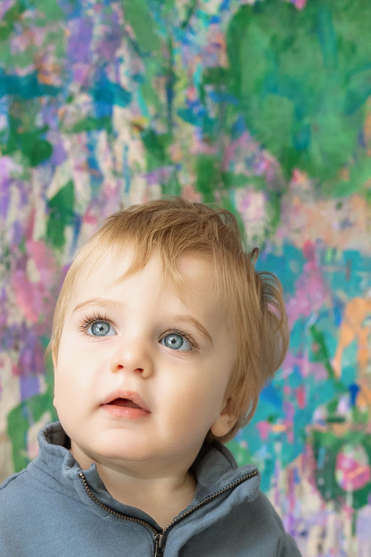 A curious toddler with blue eyes looks up against a colorful abstract painted background.