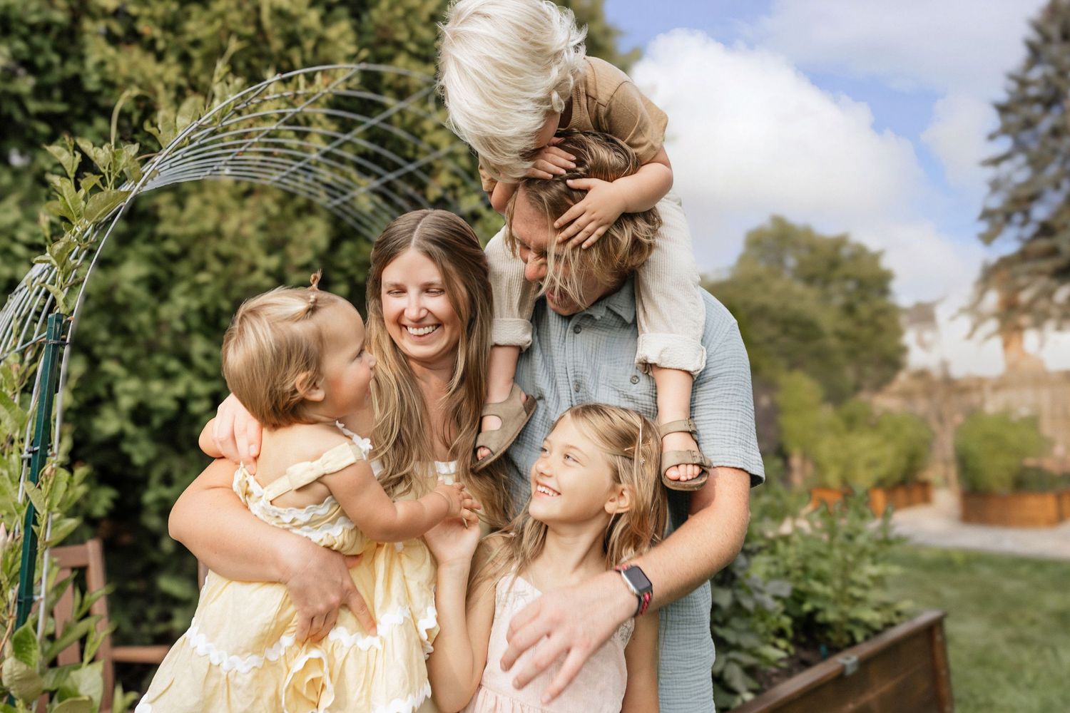 Happy family with children laughing together in a lush garden, enjoying a warm sunny day outdoors.