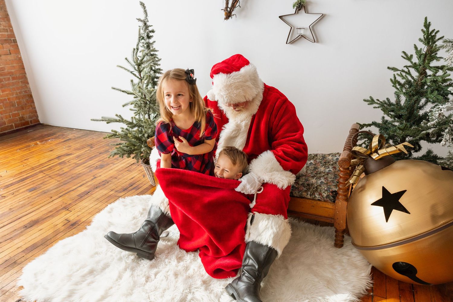 Young girl sits with Santa Claus on white fur rug surrounded by Christmas trees and decor.