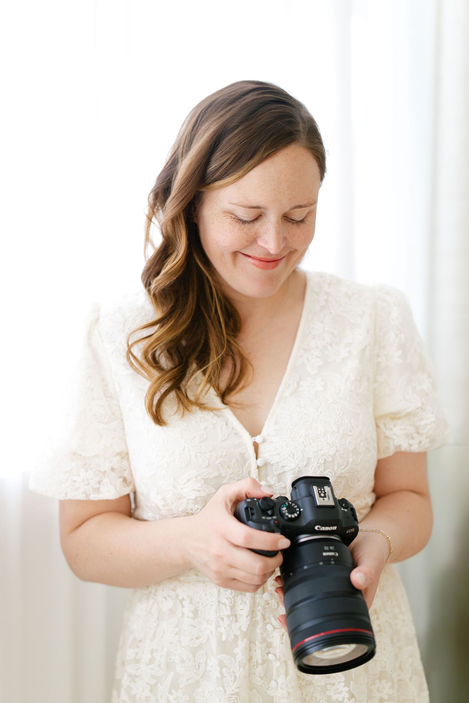 Hilary Mauro in white lace dress smiling while reviewing photos on a Canon DSLR camera.