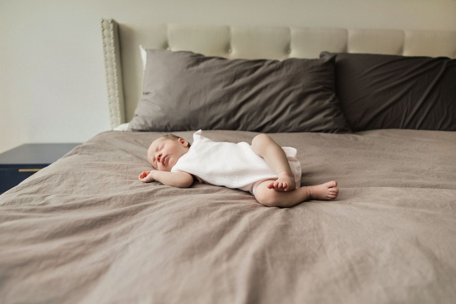 Peaceful newborn baby sleeping on a large bed in a white onesie.