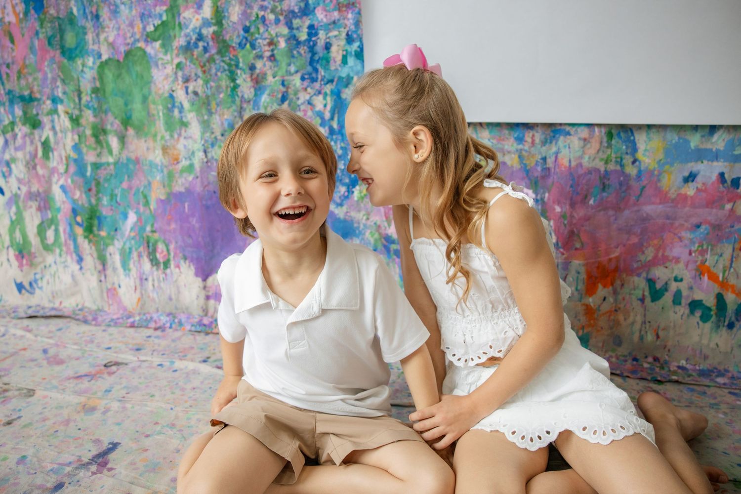 Two happy children laughing together in front of a colorful painted wall backdrop.