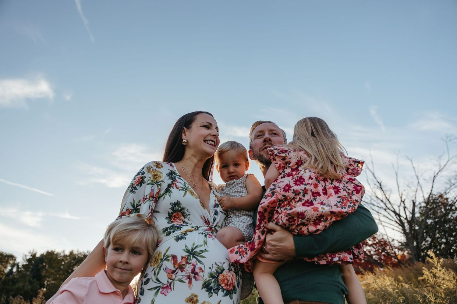 Joyful family of five with three children laughing together outdoors under a blue sky.