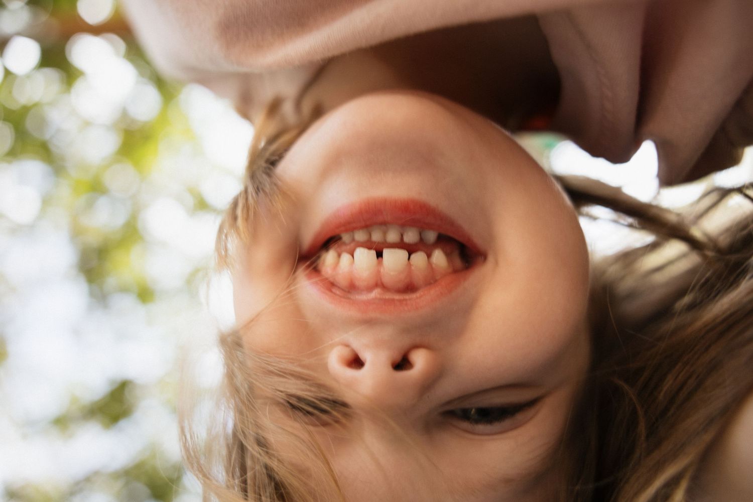 Happy young girl smiling upside down showing teeth outdoors in natural light.