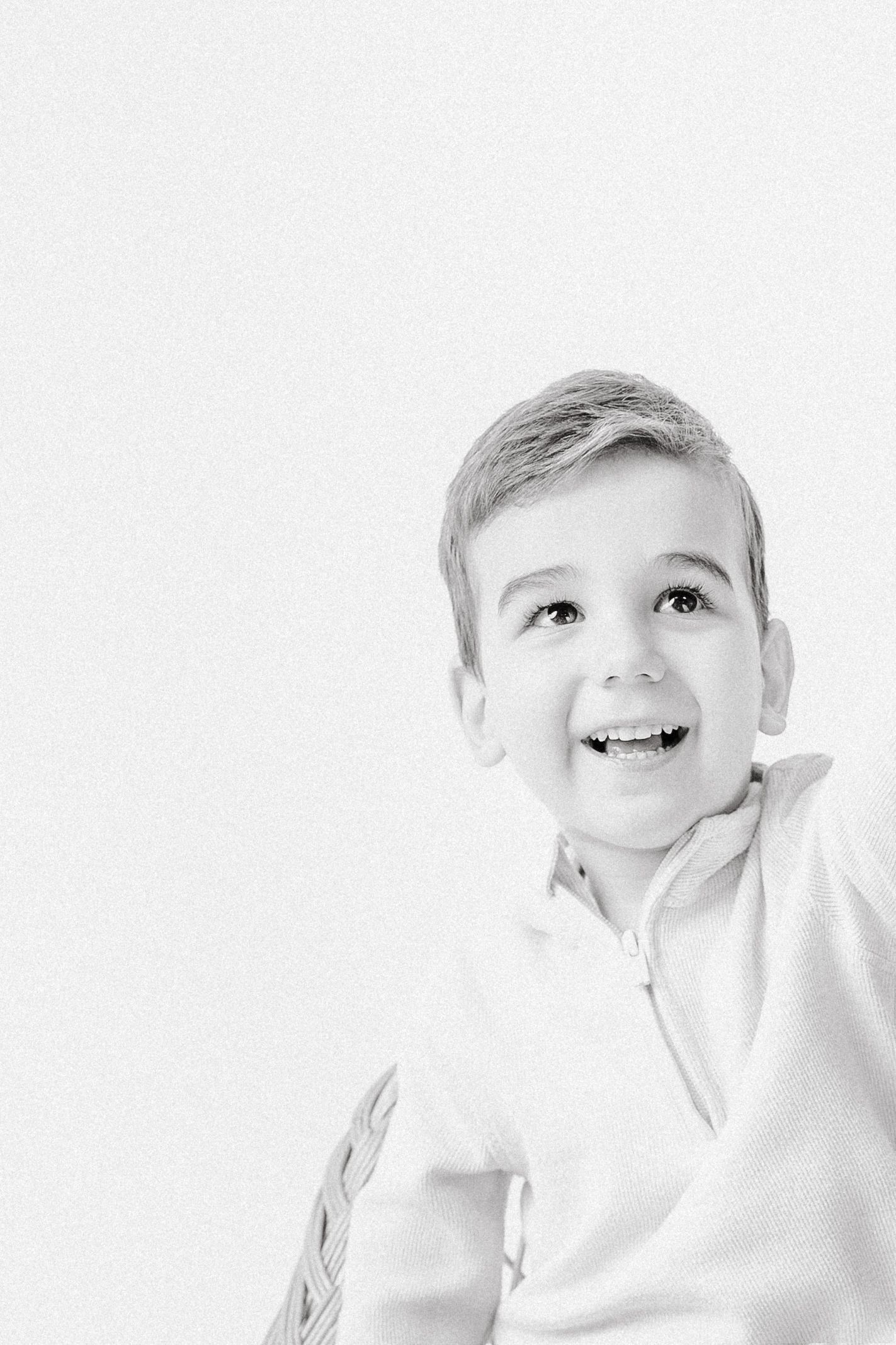Smiling young boy in white shirt looking up, black and white portrait photo.
