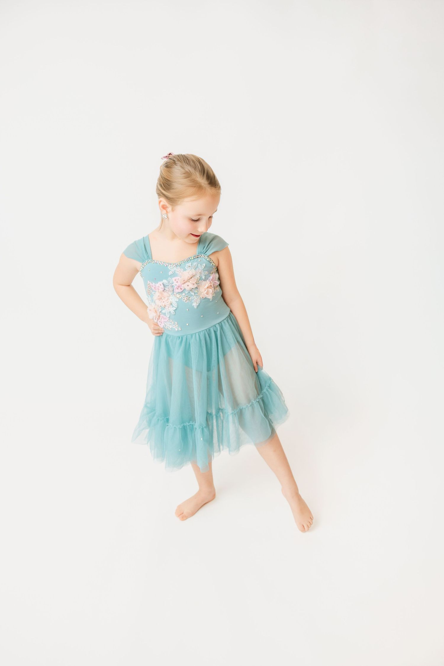 Little girl in a teal floral ballet dress dancing barefoot against a white background.