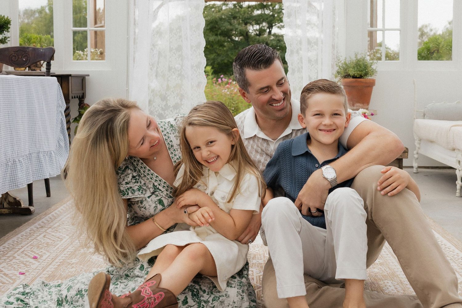 Happy family of four laughing together in a bright, cozy living room during a professional portrait session.