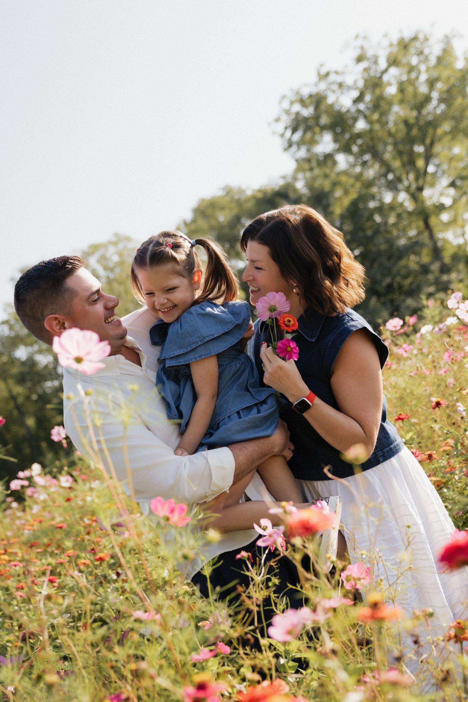 Happy family with young daughter enjoying a sunny day in a vibrant pink cosmos flower field outdoors.
