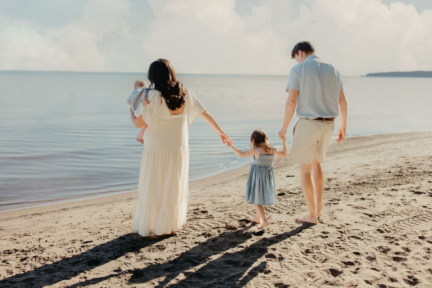 Family of four walking hand-in-hand along a peaceful sandy beach at sunset.