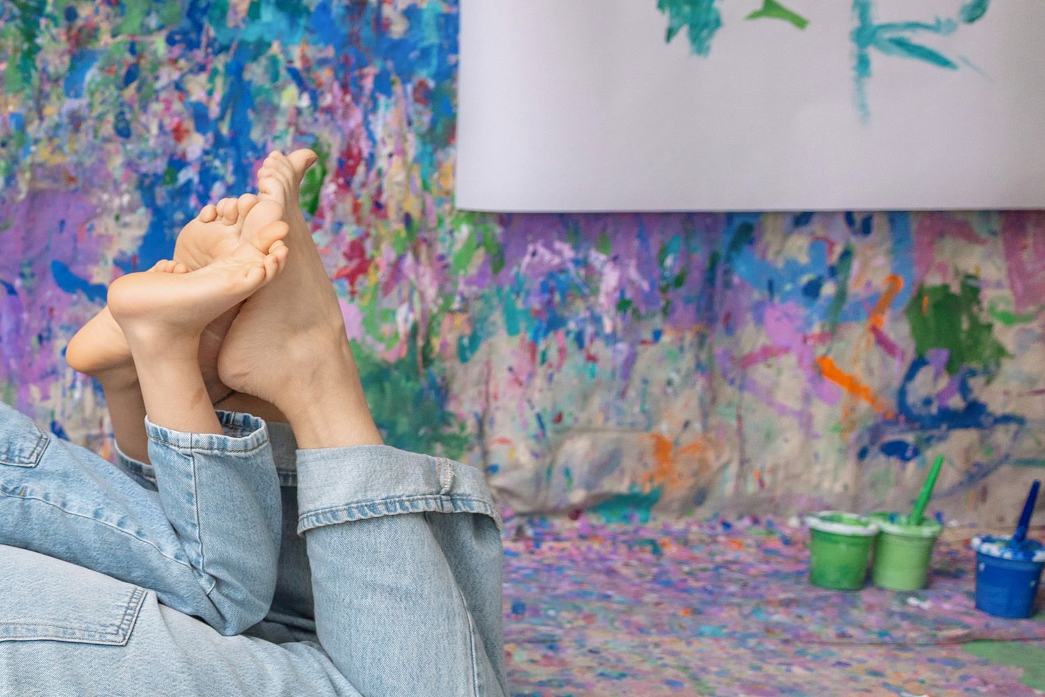 Mom and daughter relaxing with bare feet up in a colorful paint-splattered art studio.