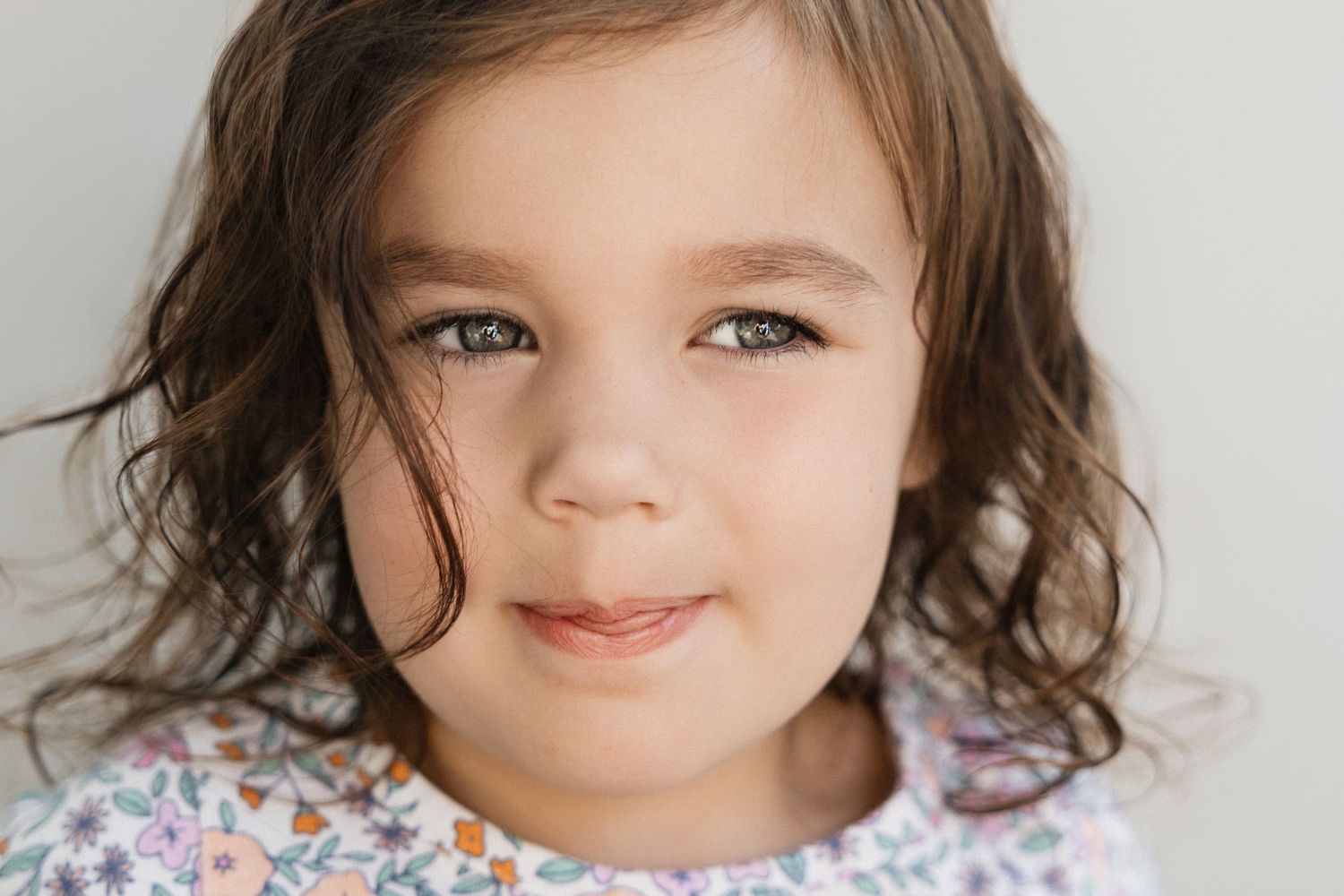 Close-up portrait of a young girl with curly brown hair and green eyes wearing a floral top.