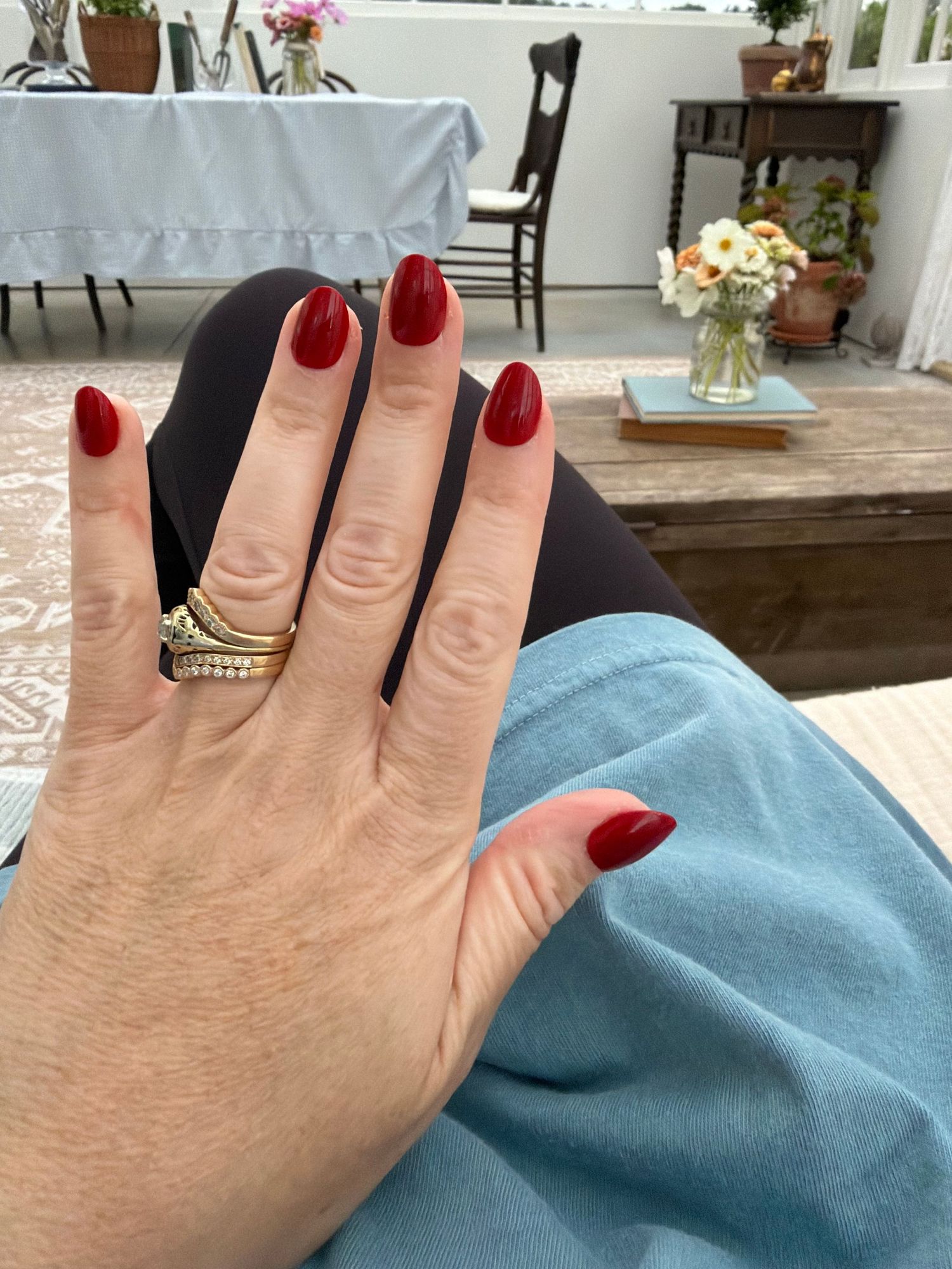 Close-up of a hand with red oval nails, wearing a diamond wedding ring set, resting on a blue denim surface.