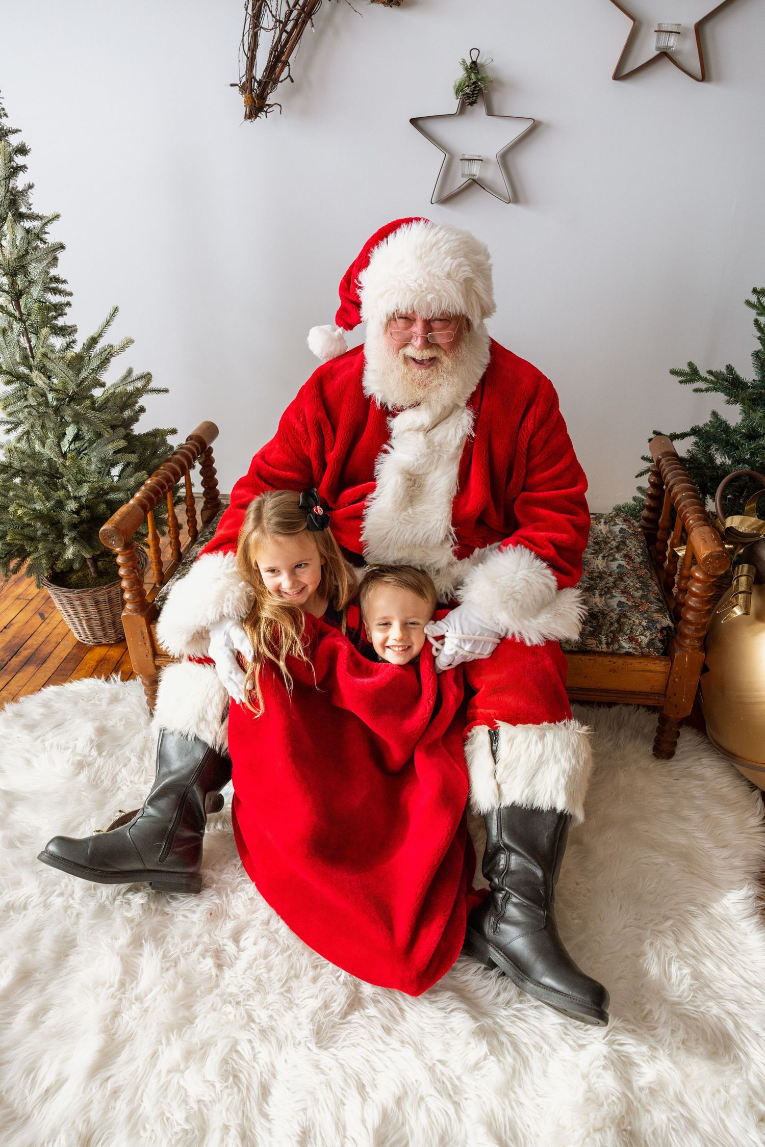 Two smiling girls in red dresses pose with Santa Claus during a festive Christmas photo session.