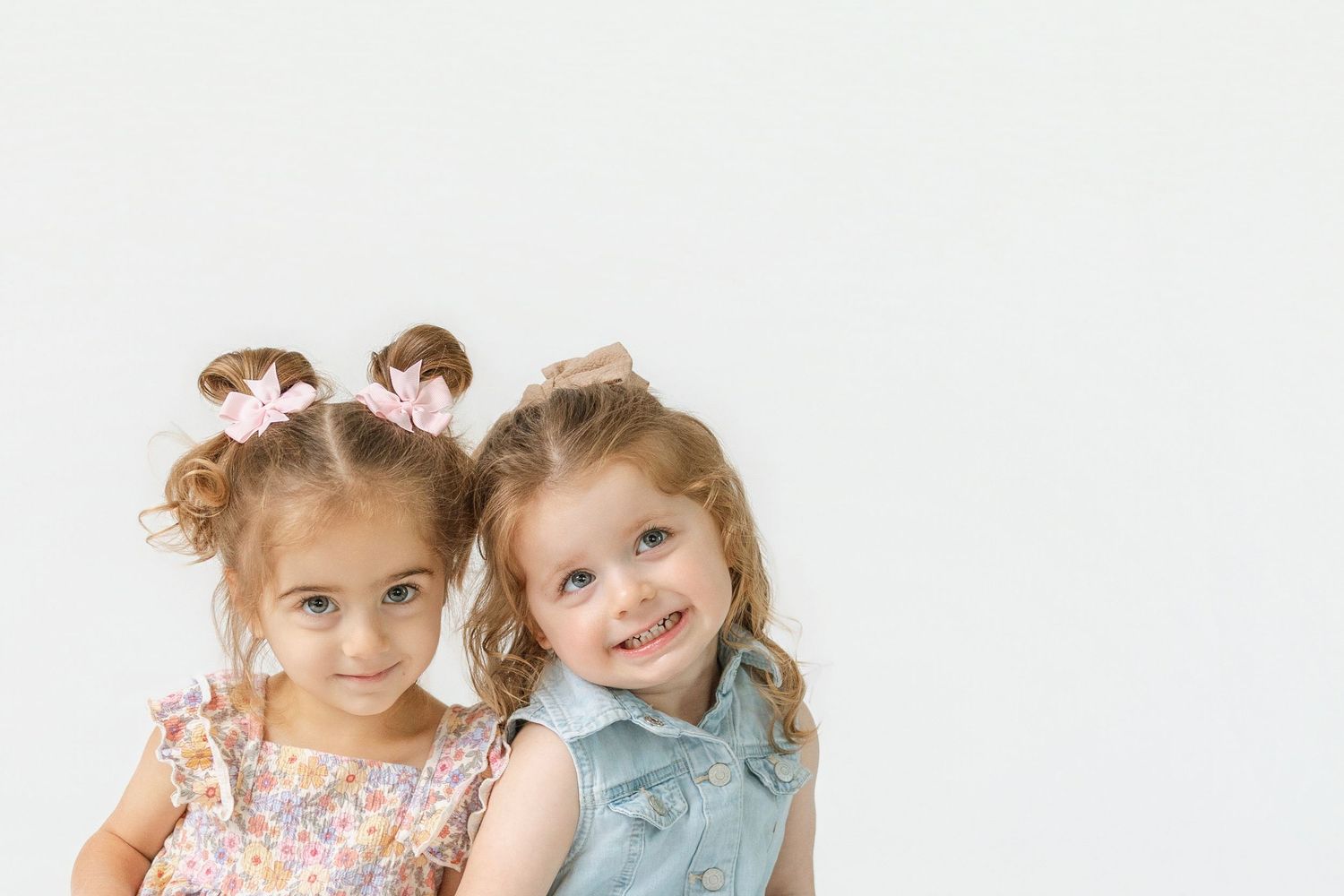 Two smiling little girls with pigtails posing together against a white background in cute dresses.
