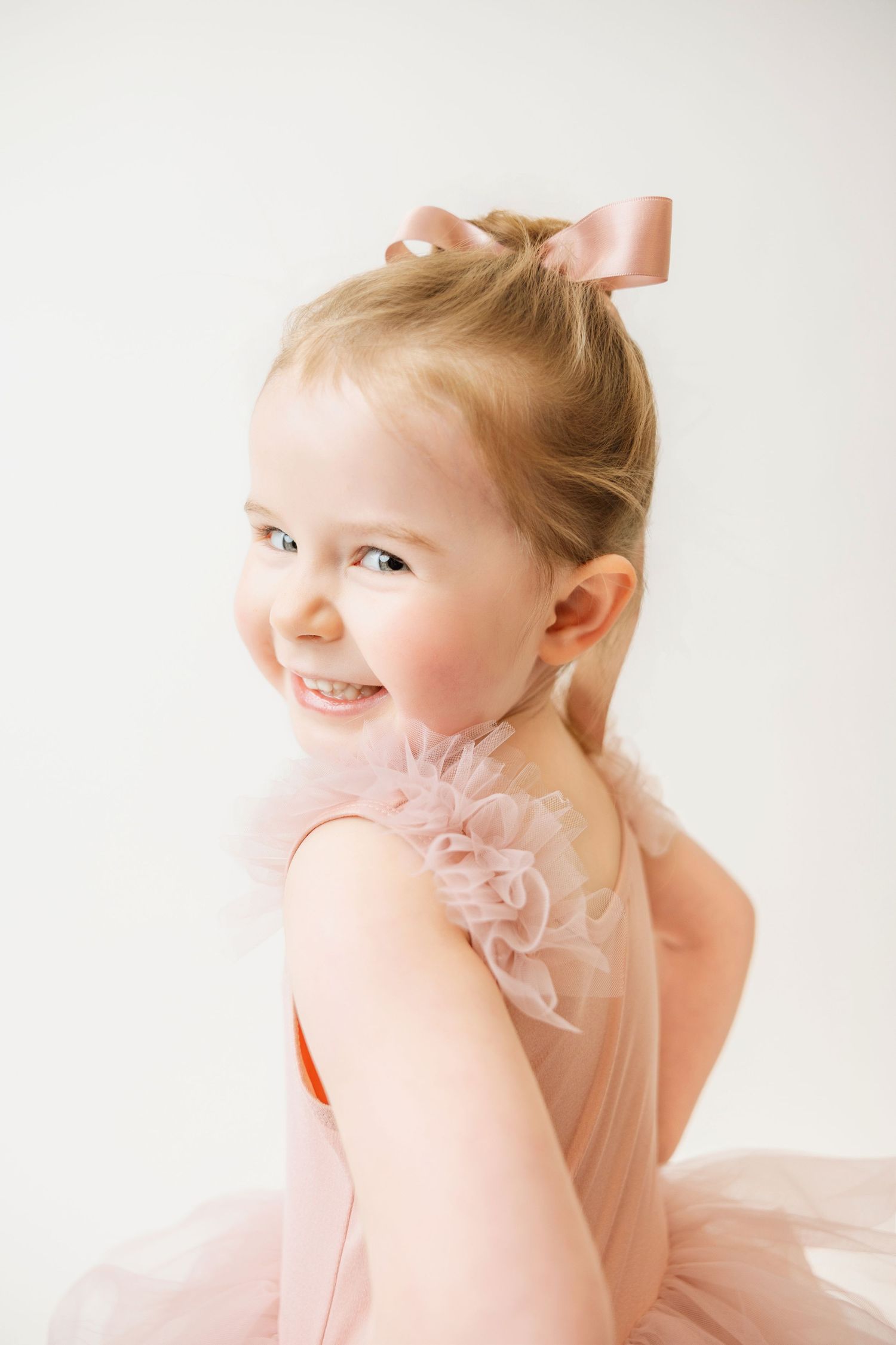 Sweet little girl in a pink tutu with satin bow smiling over her shoulder.
