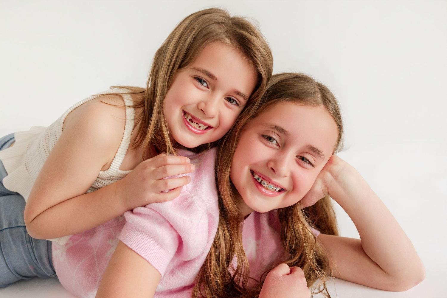 Two smiling siblings pose together playfully against a clean white background.