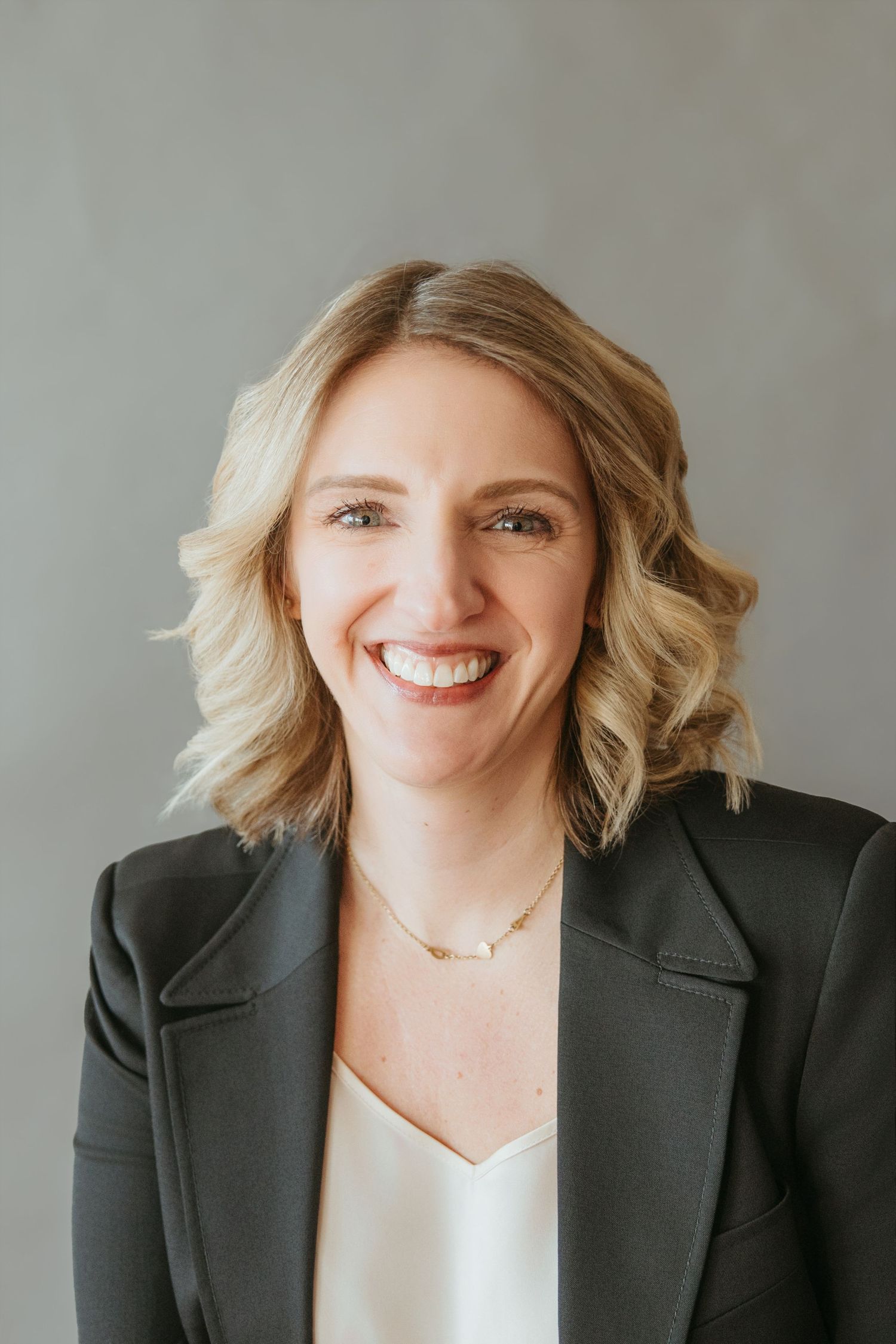 Professional blonde woman smiling in a dark blazer and white top for a business headshot.