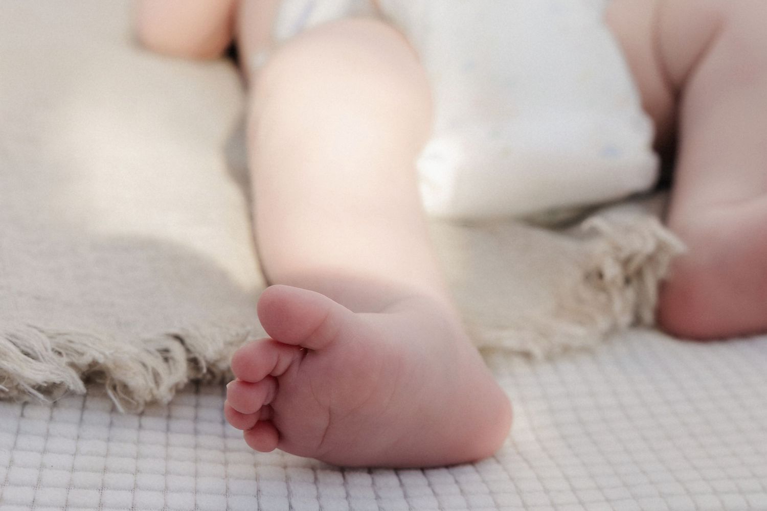 Close-up of tiny newborn baby feet resting on a soft white textured blanket with fringe.