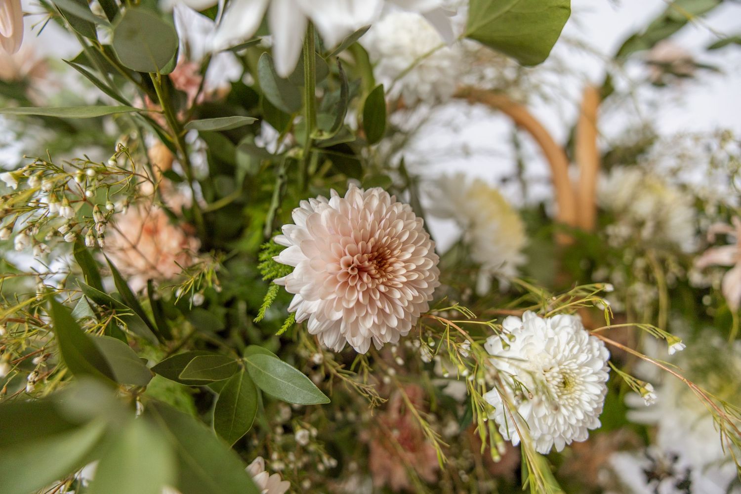 Elegant floral arrangement featuring blush pink dahlias, white blooms, and lush greenery for a romantic wedding centerpiece.