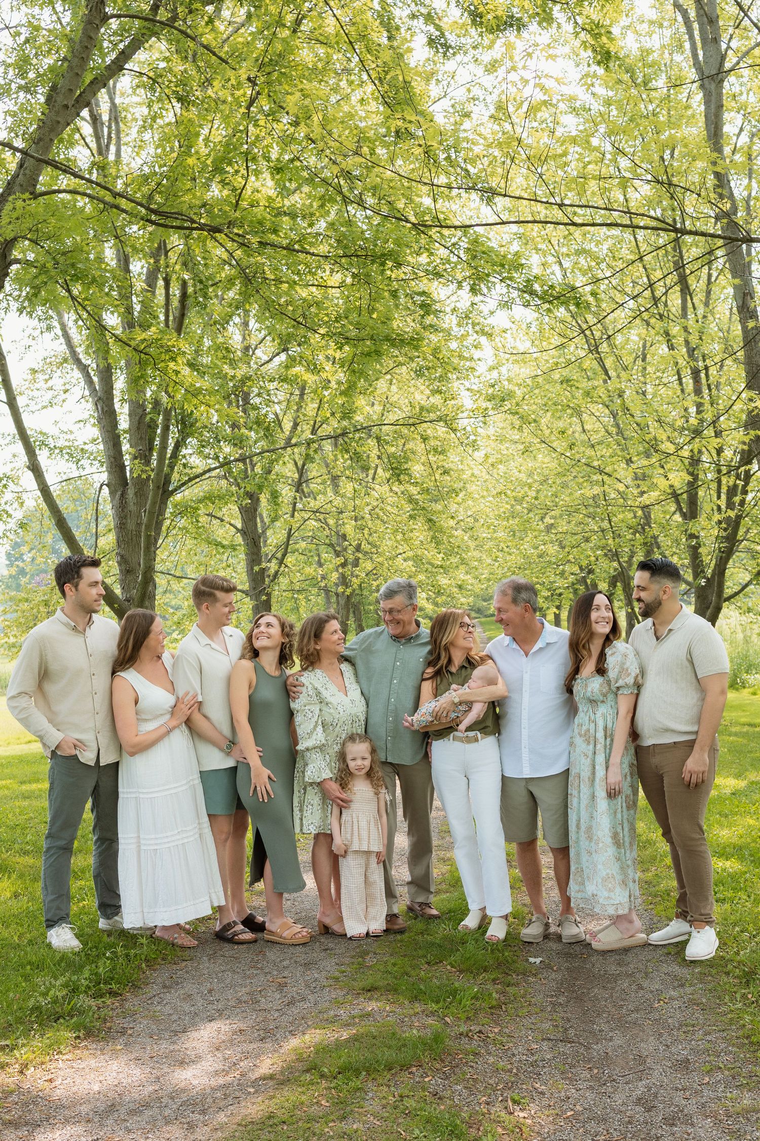 Large extended family gathered on scenic tree-lined path in summer park.