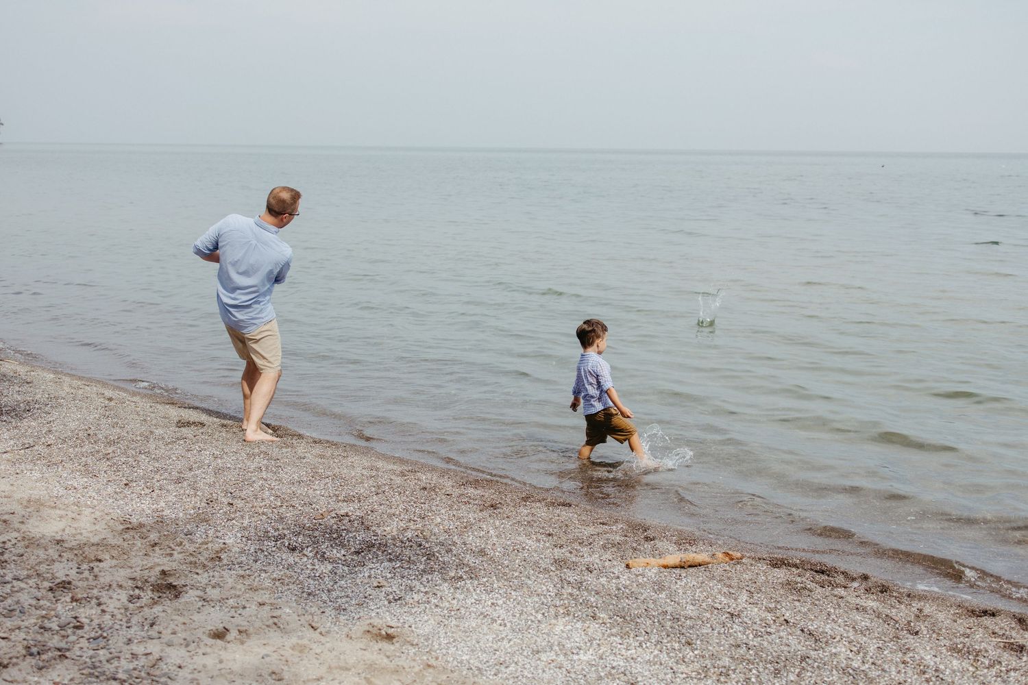 Father and child playing at rocky shoreline on calm overcast day.