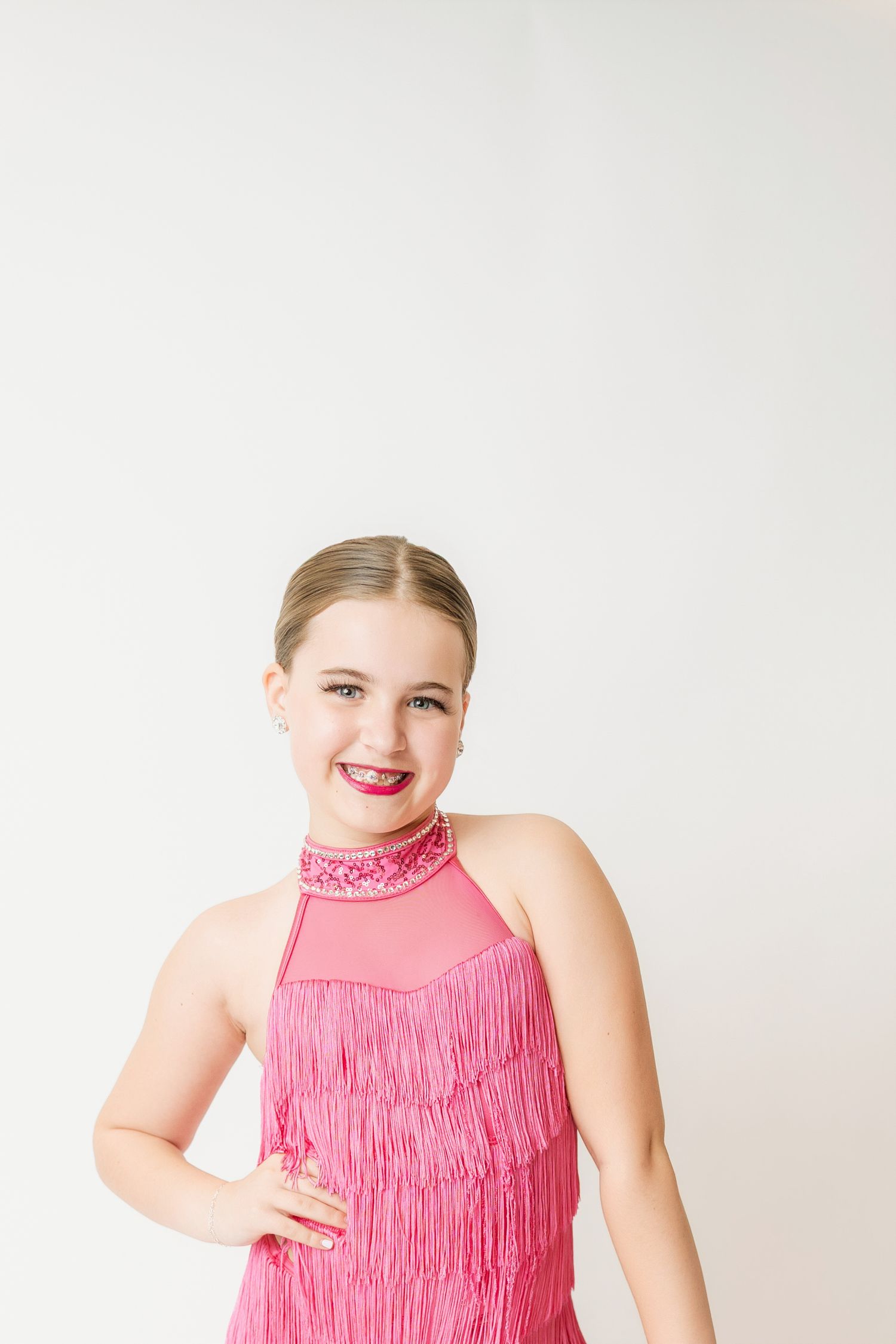 Young girl in a pink sequined fringe dance costume smiling against a white background.