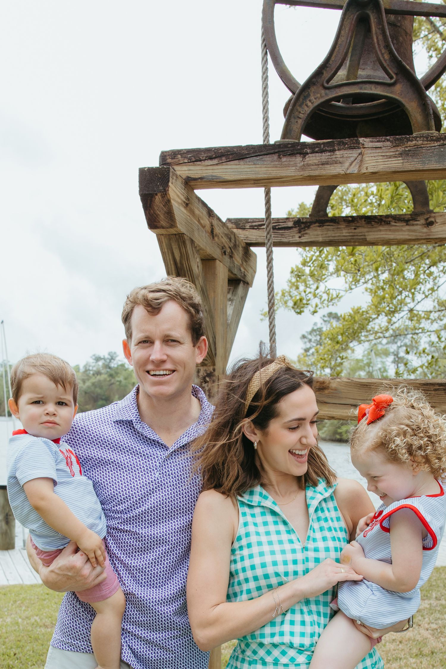 Young family of four posing near rustic wooden structure by waterfront.