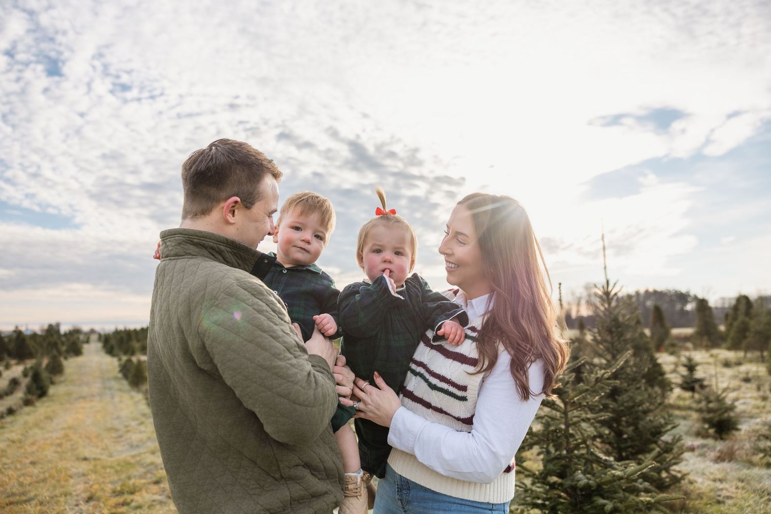 Young family with twin babies enjoying a Christmas tree farm outing on a sunny winter day.
