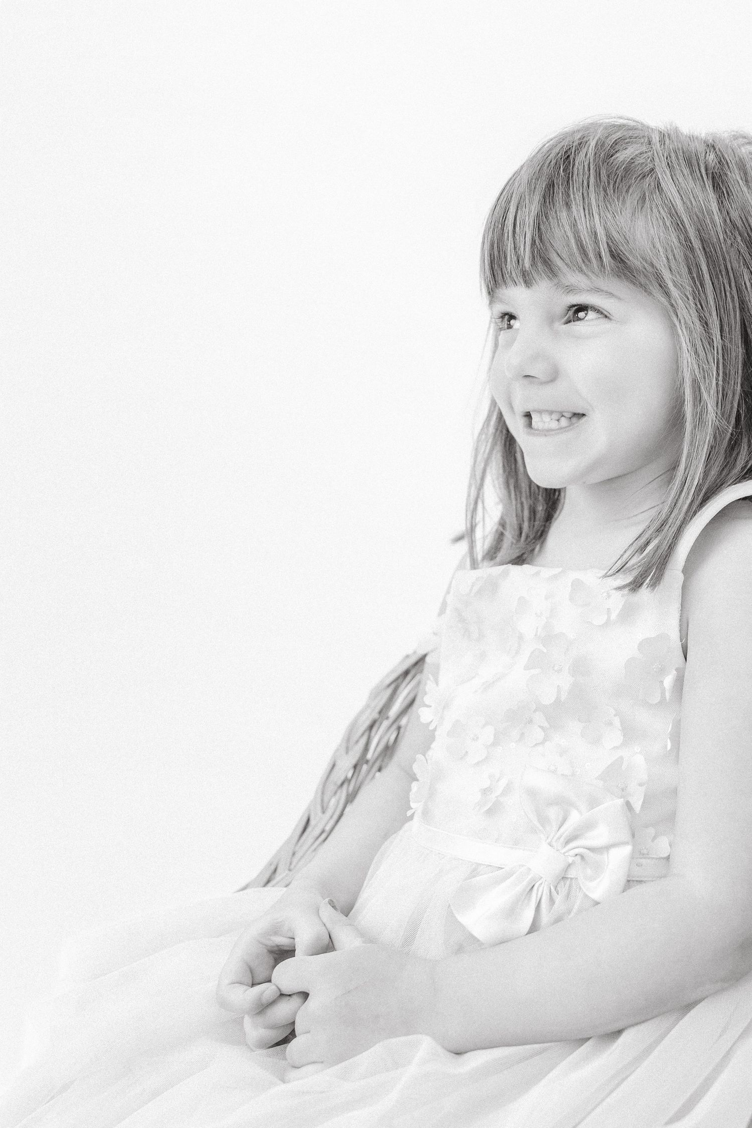 Cheerful young girl in white ruffled dress smiling in elegant black and white portrait.