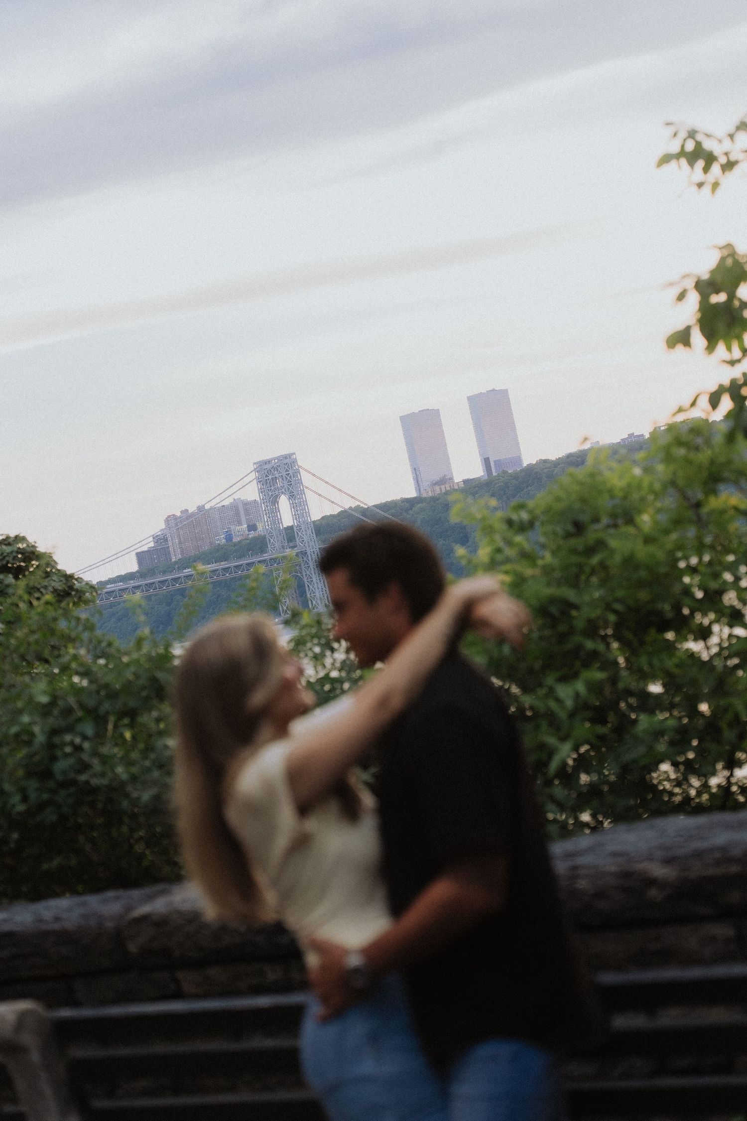 Couple dancing outdoors with George Washington Bridge and city skyline in the background.