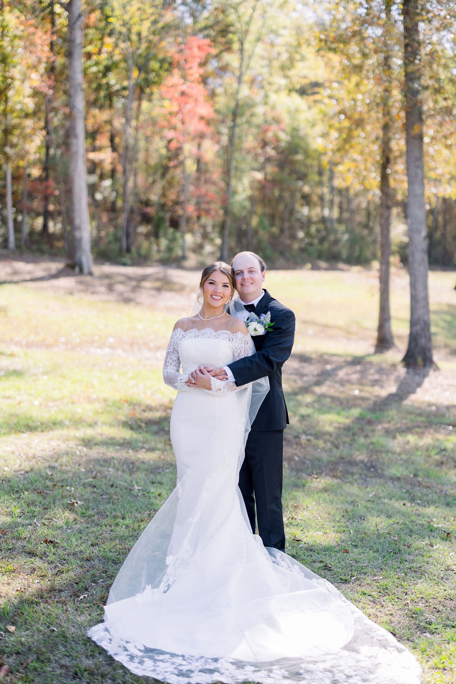 Elegant bridal portrait showcasing lace wedding dress with flowing train in autumn woodland setting.