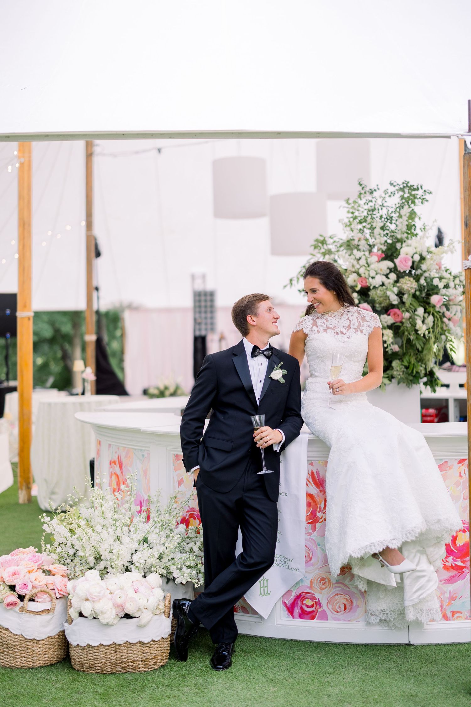 Bride and groom sharing champagne toast at elegant outdoor wedding reception with floral arrangements.