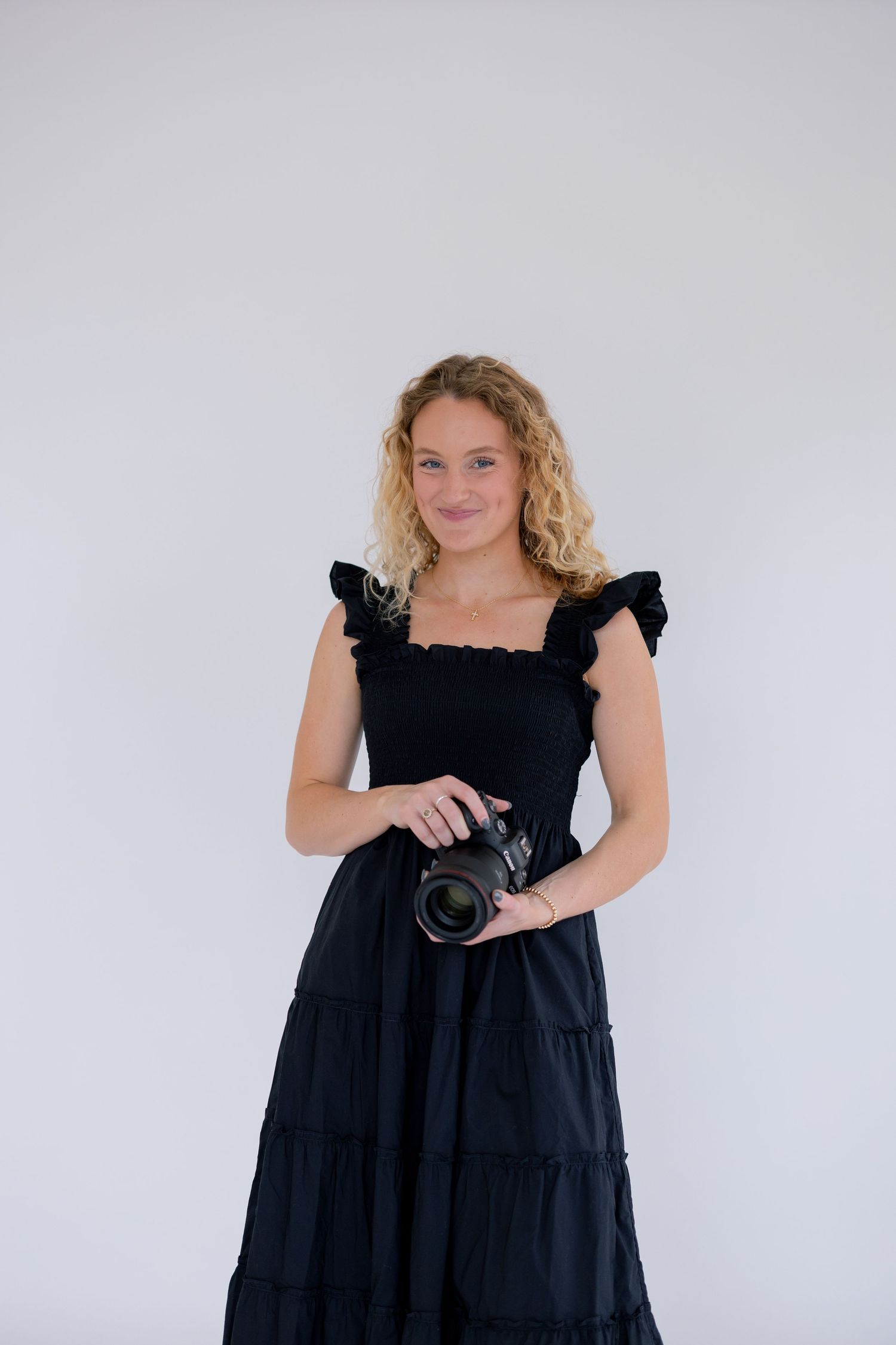 A person in a black dress poses with a camera against a white background in a series of similar shots.